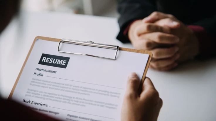 Persona mirando un CV americano mientras otra espera con los dedos entrecruzados